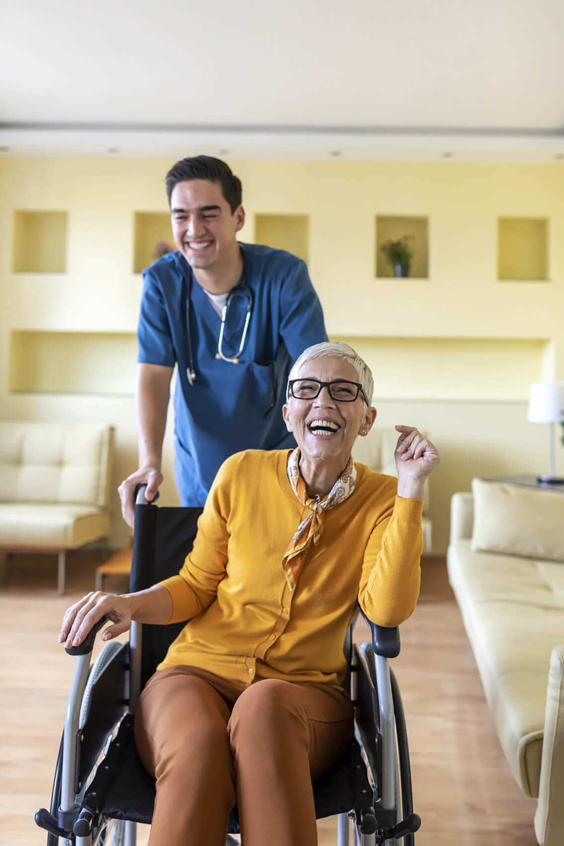 Un soignant souriant accompagnant une femme âgée en fauteuil roulant dans un environnement chaleureux