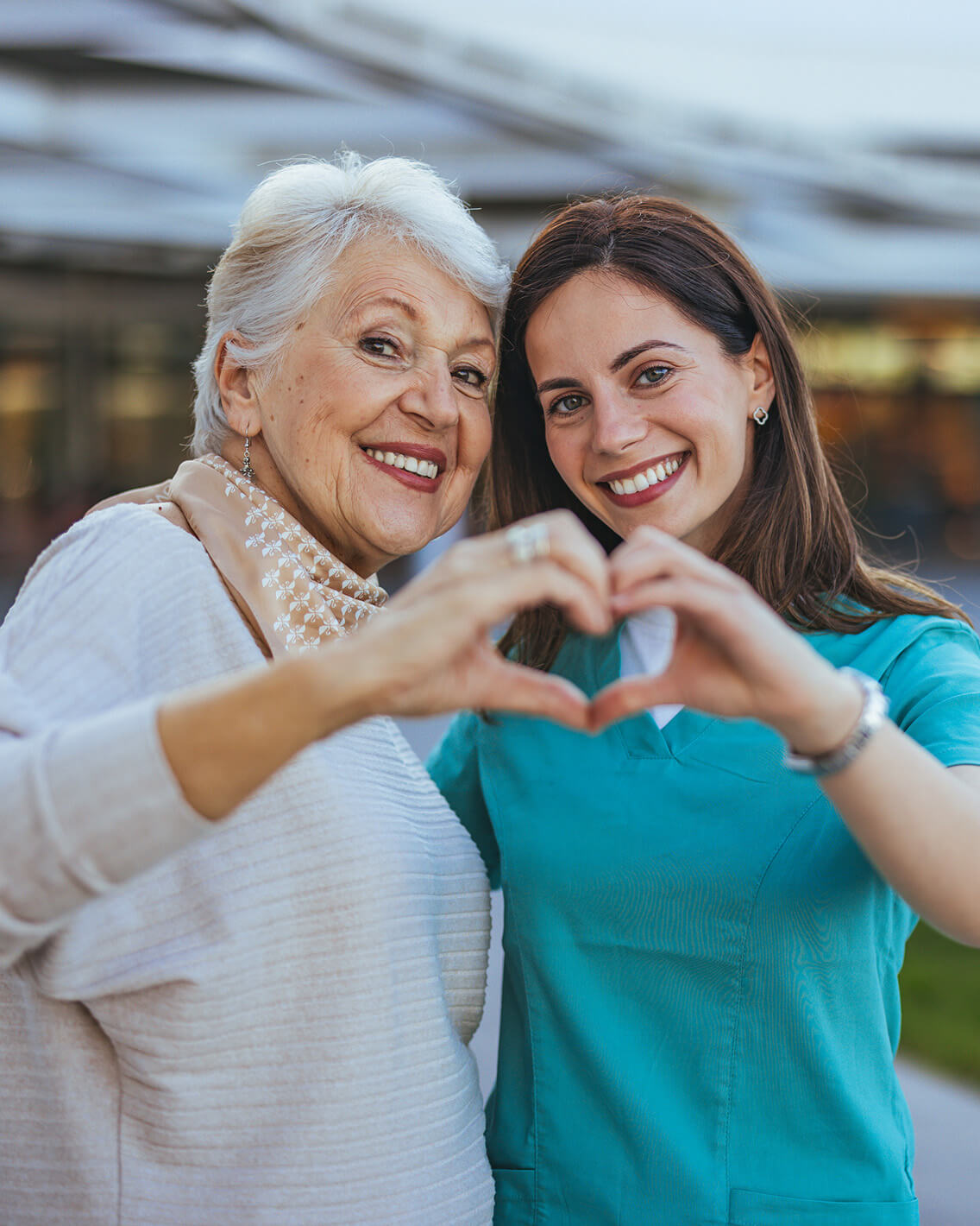 Une soignante et une femme senior formant un cœur avec leurs mains, symbolisant le soutien et l'empathie